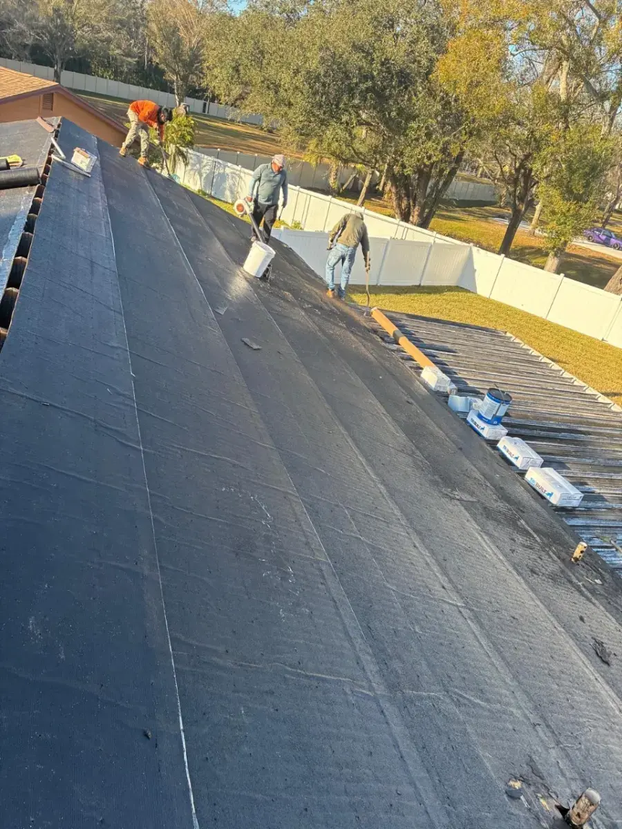 Contact Us Today Roofing crew installs black waterproof membrane on a sloped residential roof beside a fenced yard
