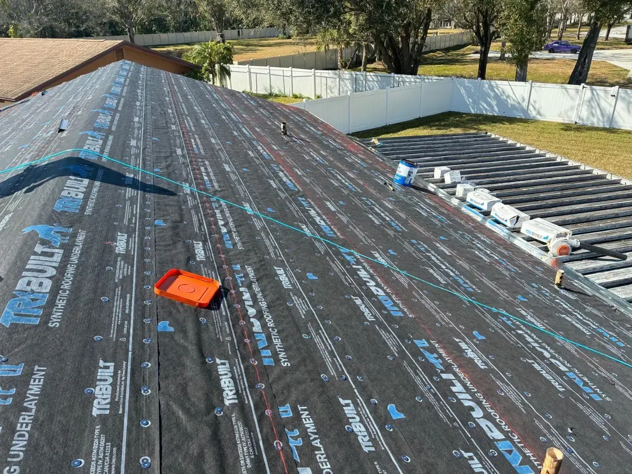 Contact Us Today Residential roof covered with synthetic underlayment, with roofing materials staged for installation